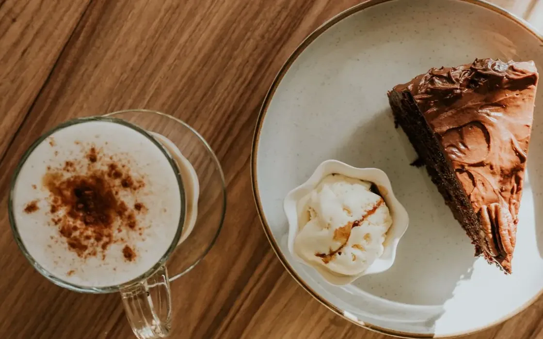 Café com canela num copo de vidro e uma fatia de bolo de chocolate com sorvete, vistos de cima na mesa de madeira
