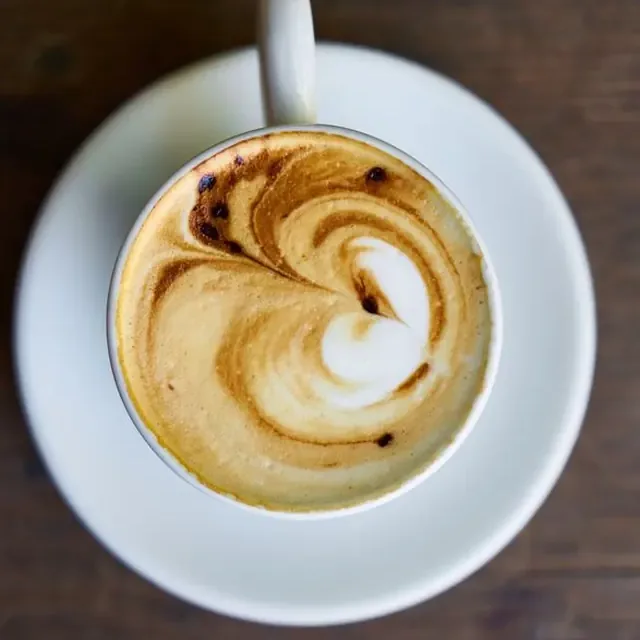 Cappuccino com desenho no leite, visto de cima, na xícara branca sobre a mesa de madeira